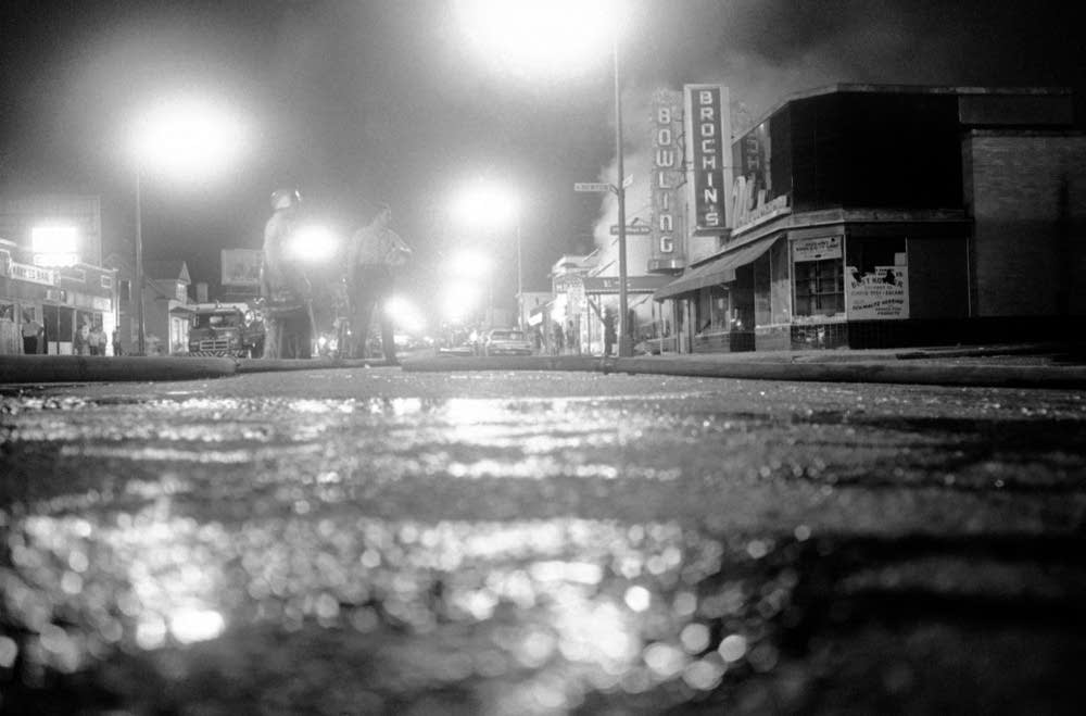 "North Minneapolis street during 1967 civil unrest, with buildings on fire and police confronting residents"